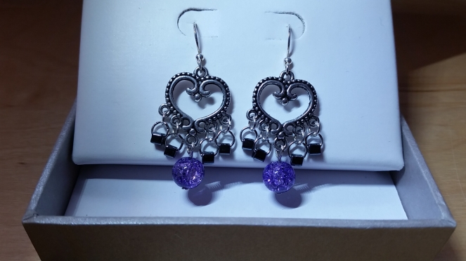 Violet Quartz and Hematite Dangle Earrings. The ear wire is longer in the back than regular length ones. There is a very cute, antiquated silver heart with 5 holes for hanging additional components, creating a V shape. The center hole has a round violet quartz hanging from it and the 4 holes going away from the quartz has a hematite cube in each of the 4 holes connected by 2 jump rings. This creates a visually appealing graduation from high to low to high again.