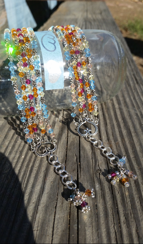 "Chasing Spring" is the name of this bracelet. It has a mix of 5 colors of Swarovski beads - aqua, orange, peach, jonquil, and fuchsia. Chasing Spring has 5 strands of colored and silver beads. They are connected to heart components at the ends. On the end of the one-inch extender dangles one of each color of the beads.